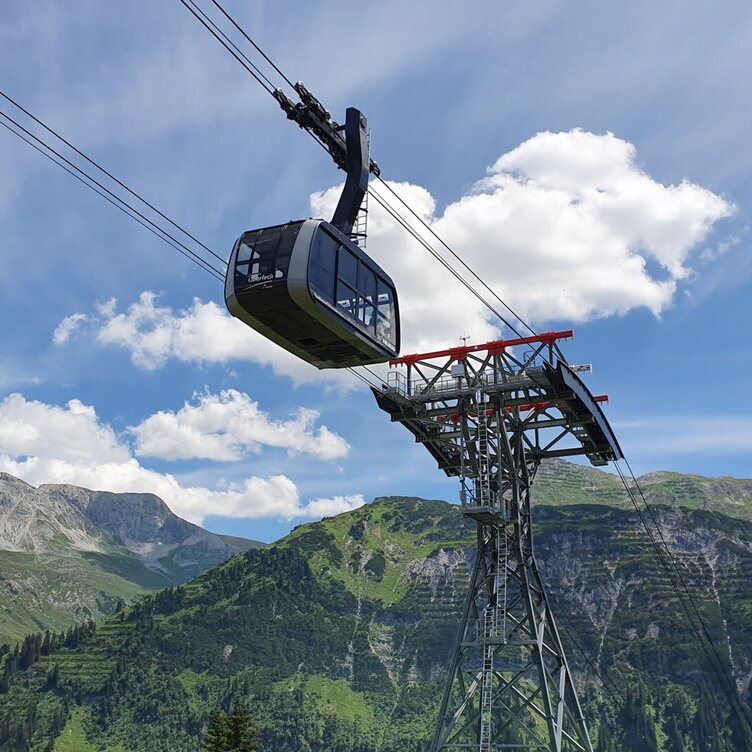 Cable car gliding above green mountains and cable tower.