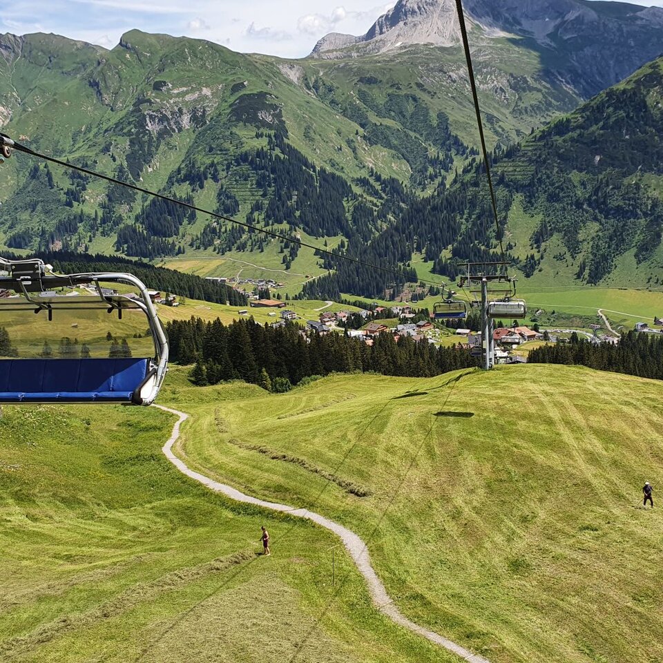Cable car over green hills with a view of Kriegerhorn and a village in the background.
