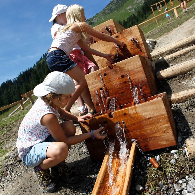 Children playing with water in wooden troughs at Kriegerhorn family mountain.