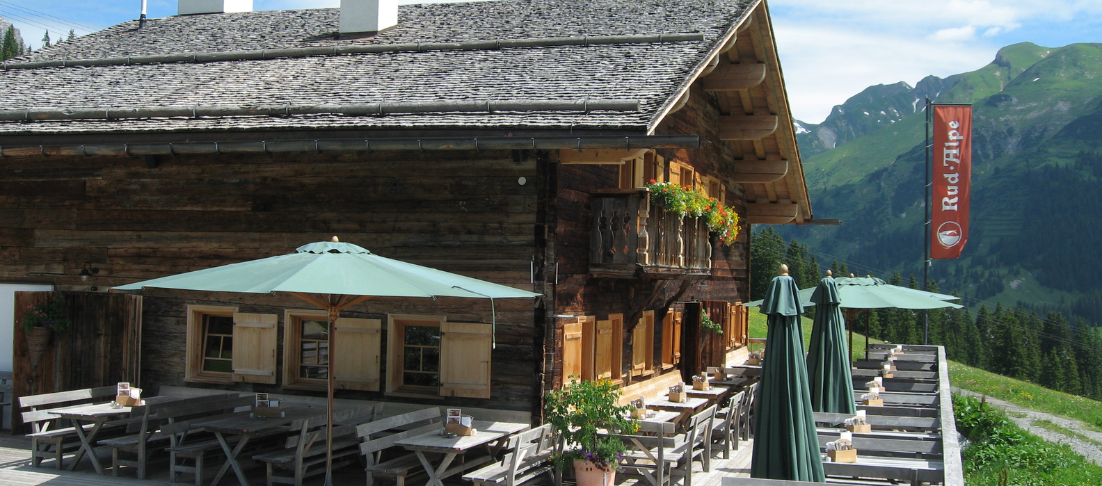 Eine Holzhütte mit Terrasse und Sonnenschirmen am Familienberg Kriegerhorn.