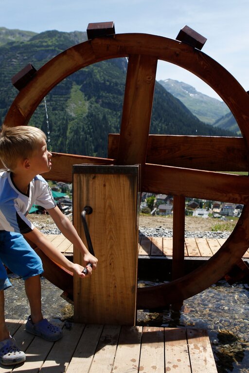 Boy playing with a waterwheel with mountain view in background.