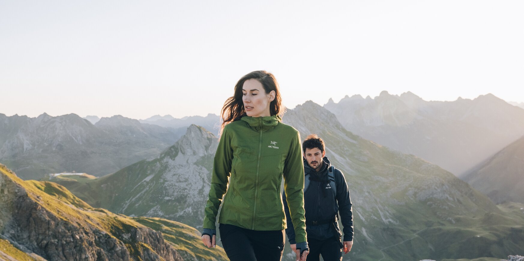 Zwei Personen wandern durch bergige Landschaft bei Sonnenaufgang.