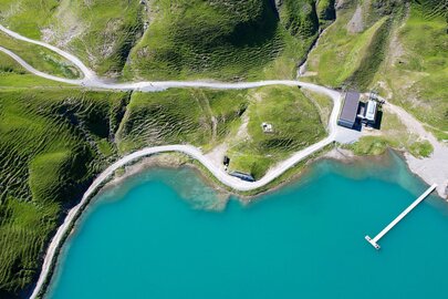 Aerial view of a turquoise lake at Seekopf nature mountain with green hills and a pier.