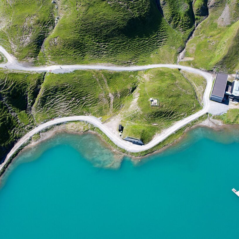 Aerial view of a turquoise lake at Seekopf nature mountain with green hills and a pier.