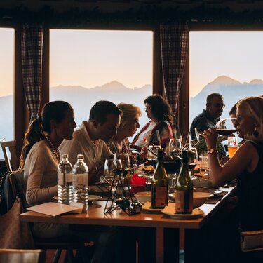A group of people enjoying dinner at Rüfikopf panoramic mountain with a sunset mountain view.
