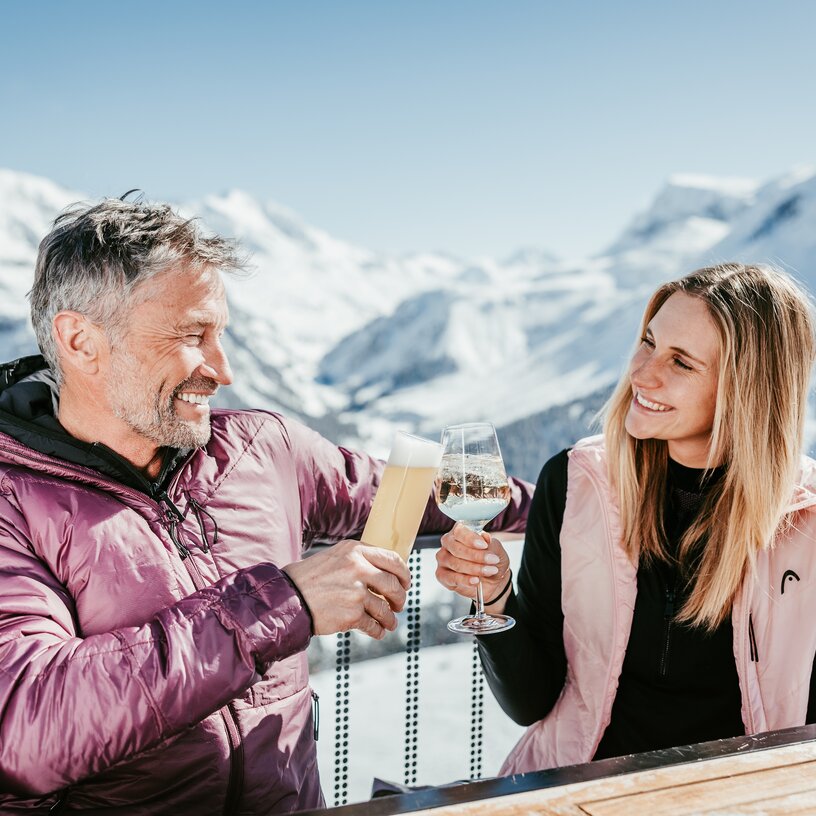 Couple enjoying drinks on terrace with mountain backdrop.