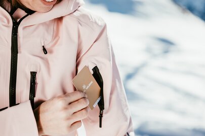Person steckt ihren Skipass von Ski Arlberg in die Ärmeltasche ihrer rosa Jacke. 