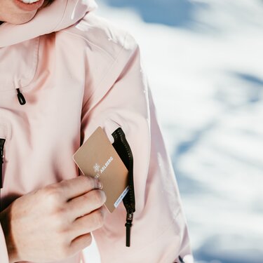 Person displaying ski pass in jacket pocket with snowy background.