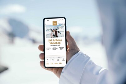 Person holding phone showing Ski Arlberg webshop page in snow.