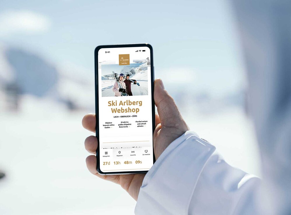 Person holding phone showing Ski Arlberg webshop page in snow.