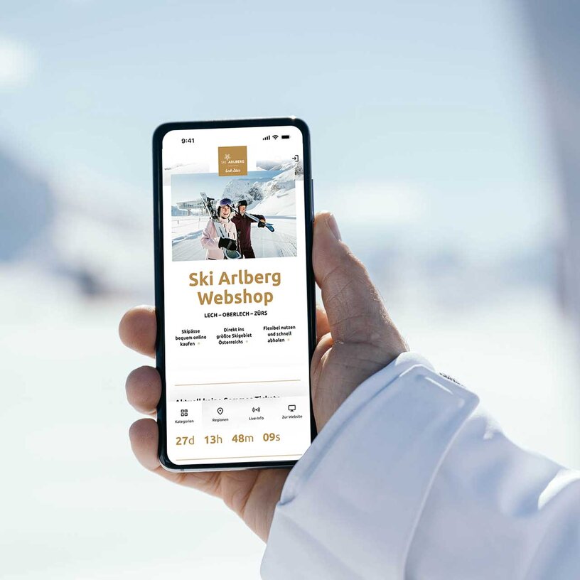 Person holding phone showing Ski Arlberg webshop page in snow.