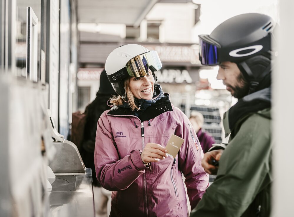 Two people in ski gear standing at a ticket counter.