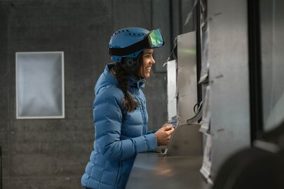 Frau in blauer Jacke und Helm kauft Liftkarte an der Kasse.