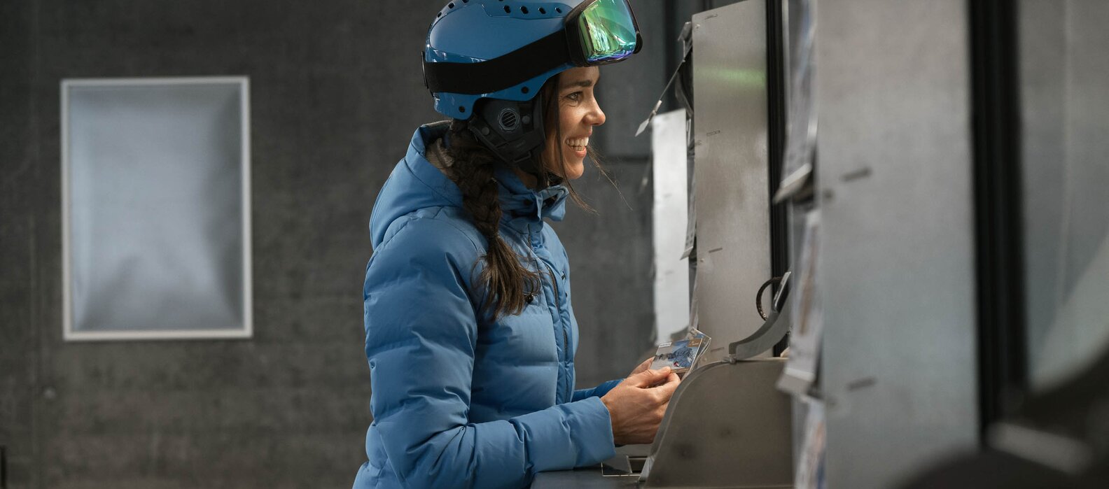 Frau in blauer Jacke und Helm kauft Liftkarte an der Kasse.