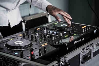 Nahaufnahme der Hände von einem DJ, der am Mischpult die Musik steuert.