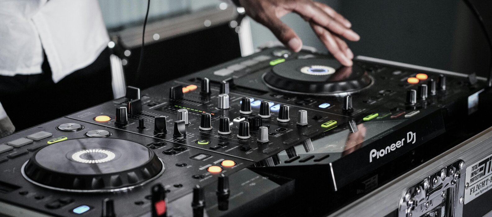 Nahaufnahme der Hände von einem DJ, der am Mischpult die Musik steuert.