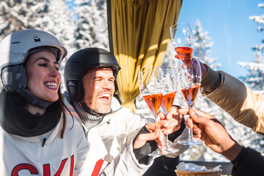 Skifahrer fahren in einer Gondel und stoßen mit Champagner an.