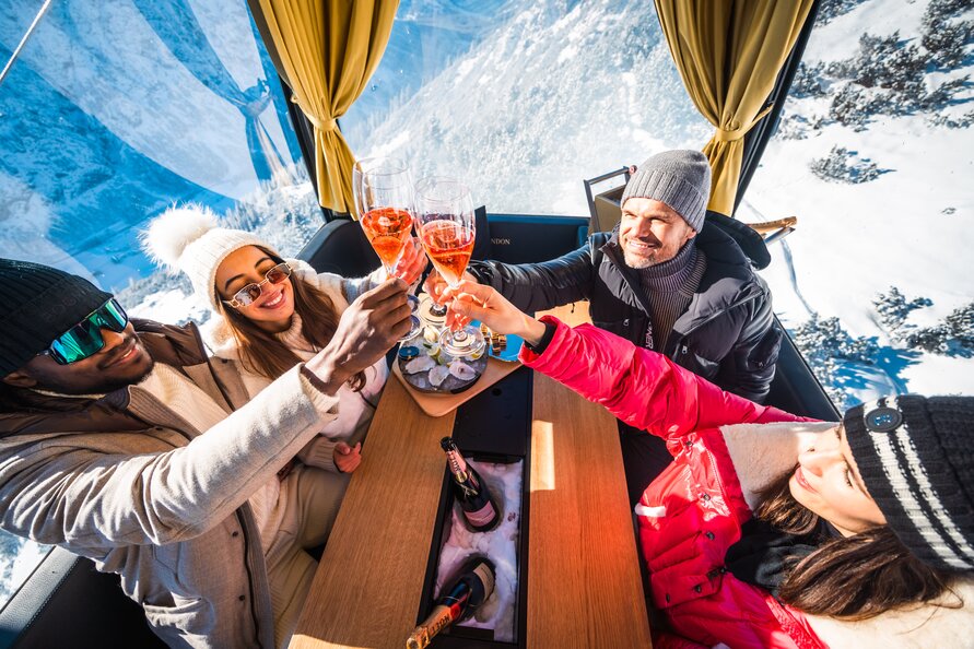 Vier Personen stoßen in einer Gondel mit Champagner an.