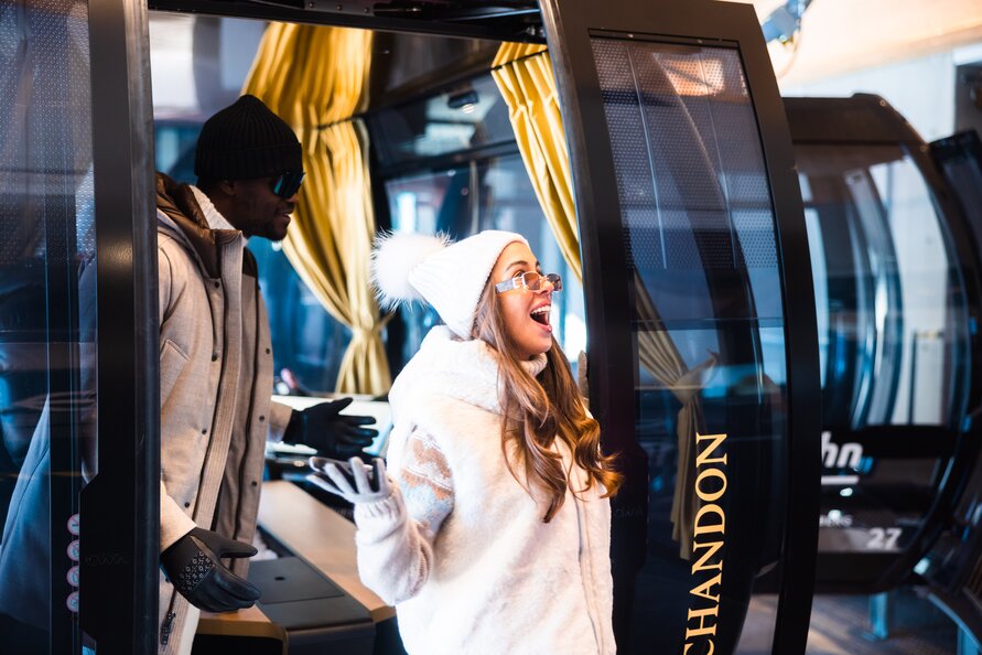 Zwei Personen in der Gondel. Sie trägt weiße Winterkleidung und ist begeistert; er trägt dunkle Kleidung.