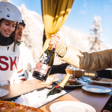 People in ski gear enjoying champagne in the gondola.