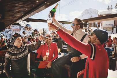 Gruppe von Männern stoßen mit Sekt an einer Ski-Bar an.