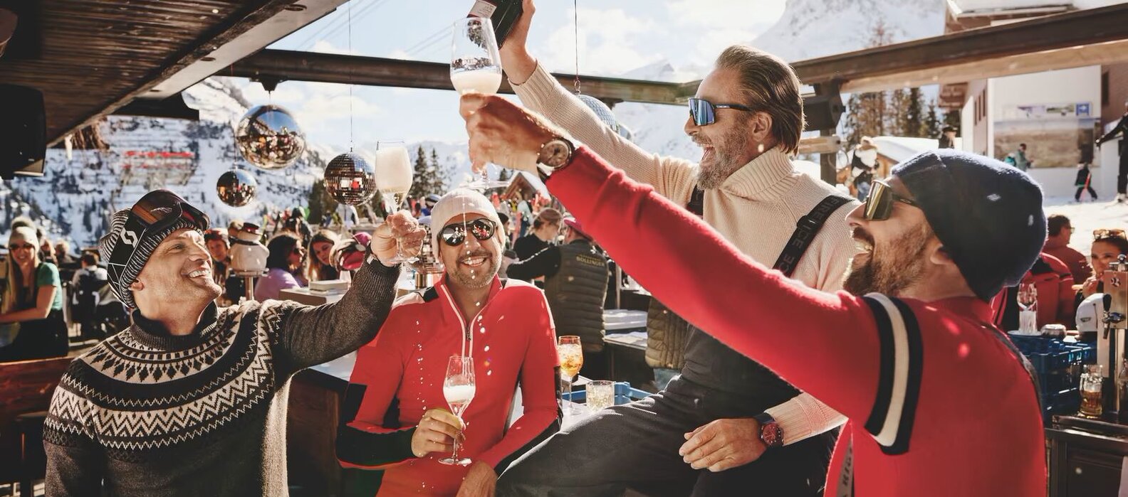 Gruppe von Männern stoßen mit Sekt an einer Ski-Bar an.