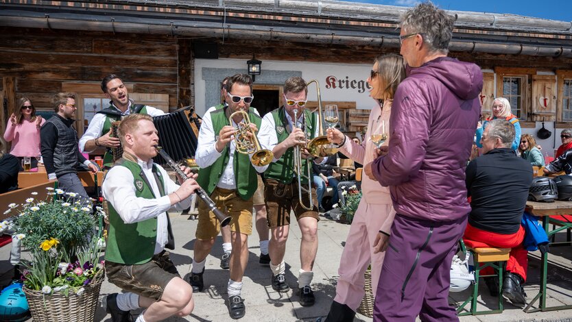 Blaskapelle in traditioneller Kleidung spielt vor Almhütte.