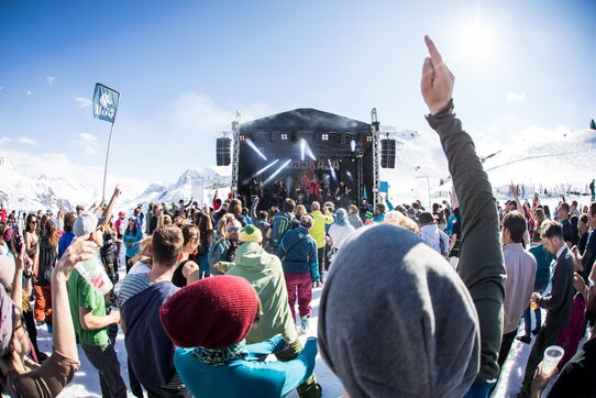 Menschen feiern bei einer Outdoor-Konzertbühne im Schnee.