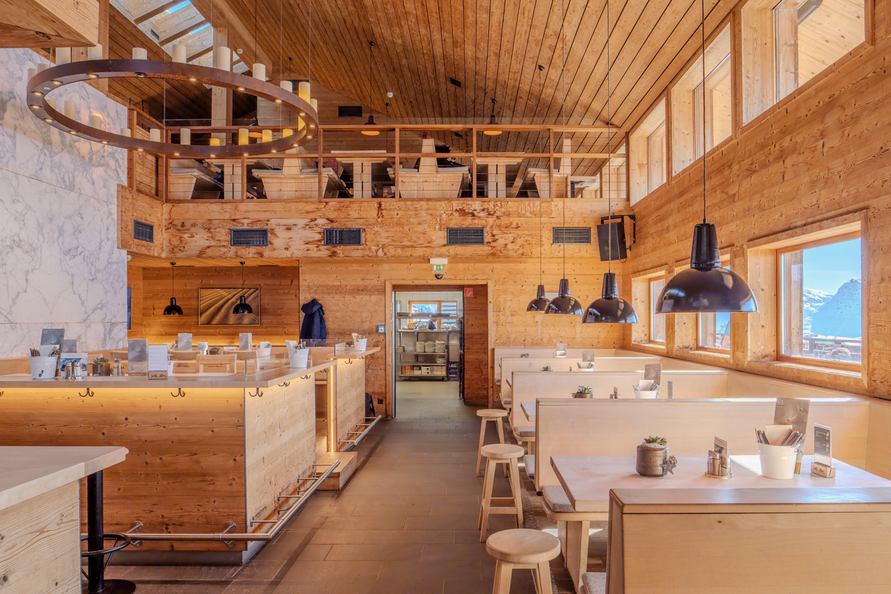 Innenansicht eines gemütlichen, holzverkleideten Restaurants 'Balmalp' mit Sitzbänken und Bar.