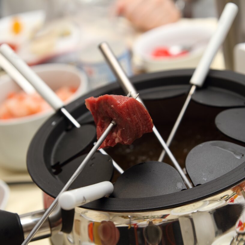 Gabeln mit rohem Fleisch in einem Fondue-Topf im Rüfikopf Restaurant.
