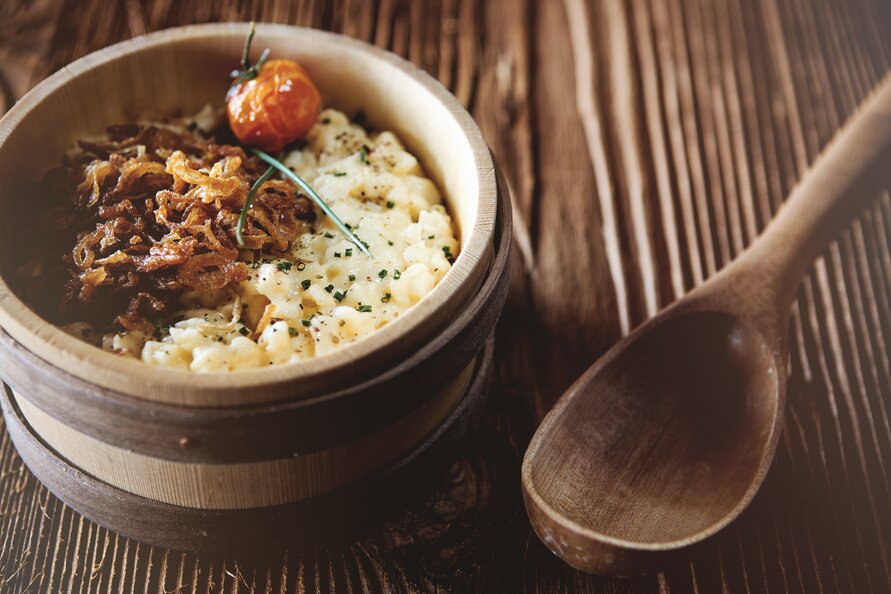 Ein hölzernes Schälchen mit Käsespätzle, garniert mit Röstzwiebeln und einer Kirschtomate, serviert im Seekopf Restaurant.