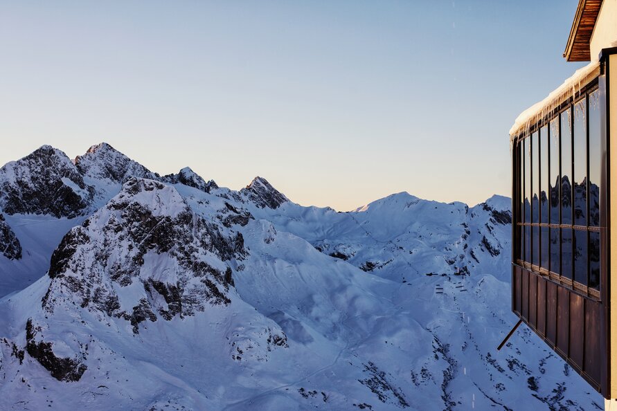 Panoramafenster von der Trittkopf BBQ Station vor verschneiter Berglandschaft bei Sonnenaufgang.