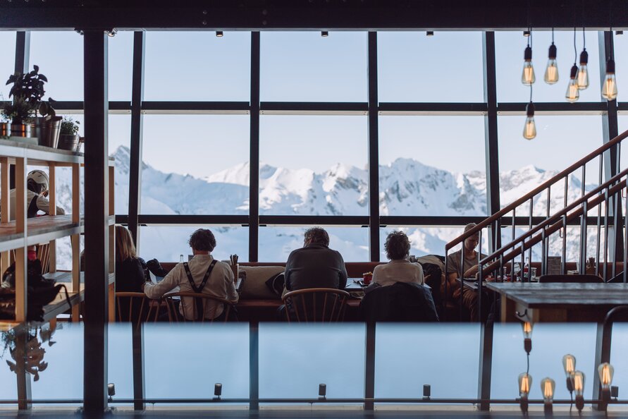 Menschen sitzen vor der riesigen Glasfront im Restaurant Trittkopf BBQ Station .