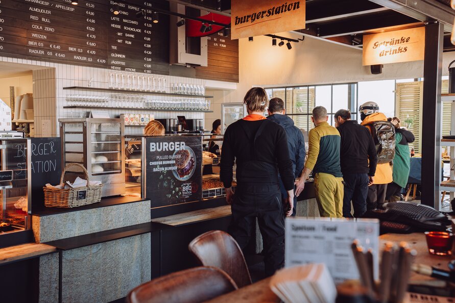 Menschen stehen in der Schlange an Essensausgabe der Trittkopf BBQ Station.