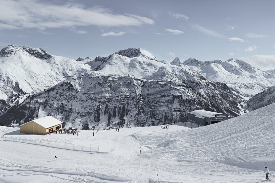 Restaurant Der Wolf inmitten schneebedeckter Berge und Skifahrern.