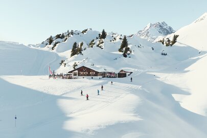 Skihütte Kriegeralpe in verschneiter Berglandschaft mit Skifahrern