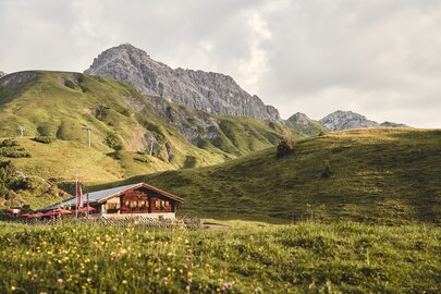 Grüne Wiesen und das Restaurant Kriegeralpe mit Bergen im Hintergrund.