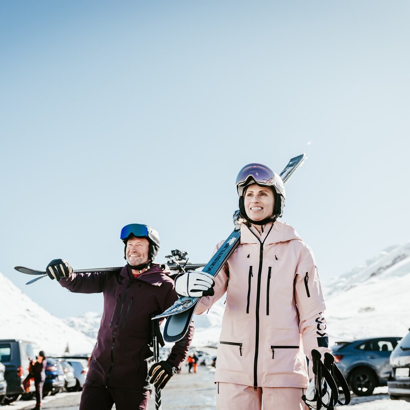 Two people in ski gear on a mountain parking lot.