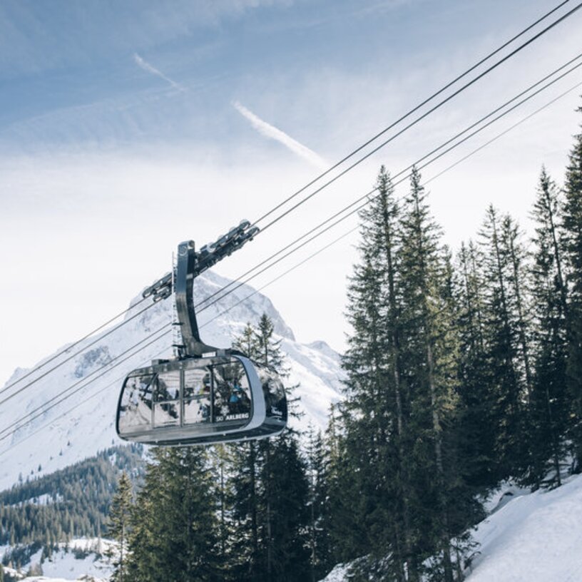A cable car above snow-covered trees with a mountain backdrop.