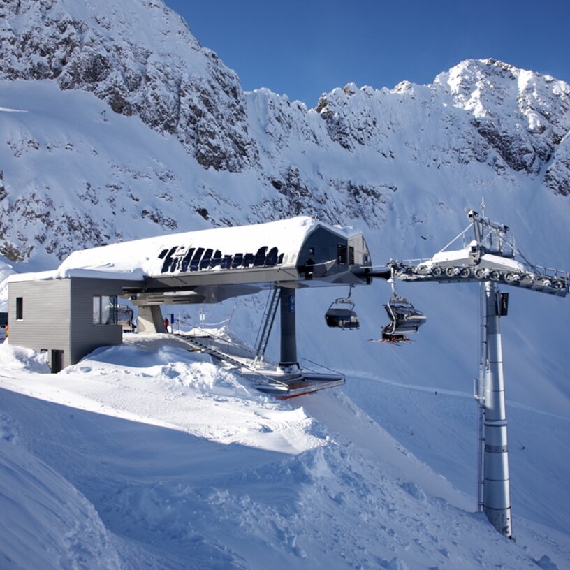 Schneebedeckte Bergstation mit Seilbahn und Bergen im Hintergrund.