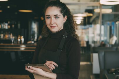 Junge Kellnerin mit Notizblock in einem stilvollen Café.