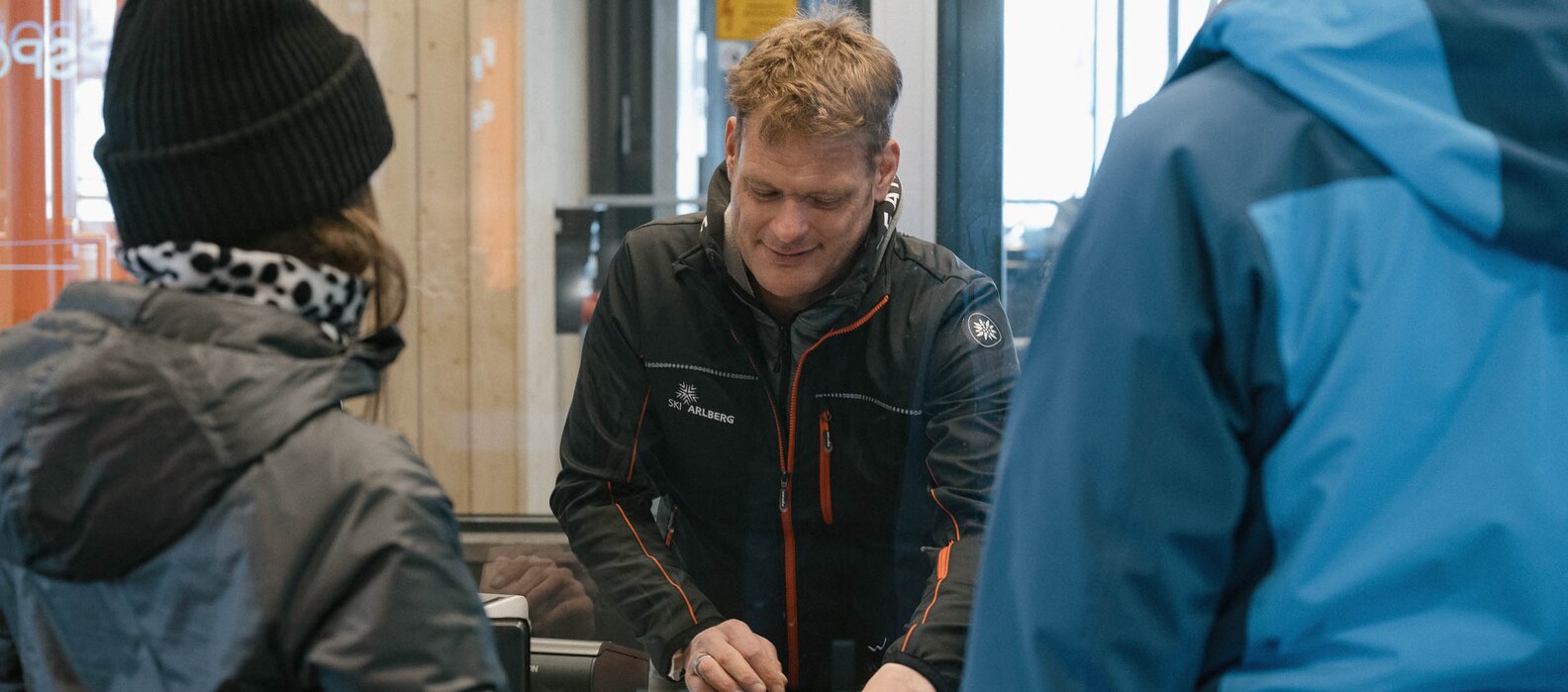 Menschen kaufen Tickets an einem Skischalter in einer Hütte.