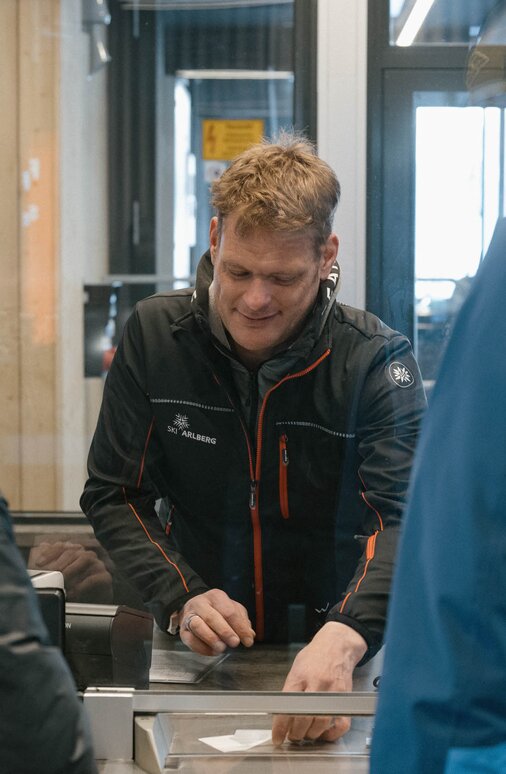 Menschen kaufen Tickets an einem Skischalter in einer Hütte.