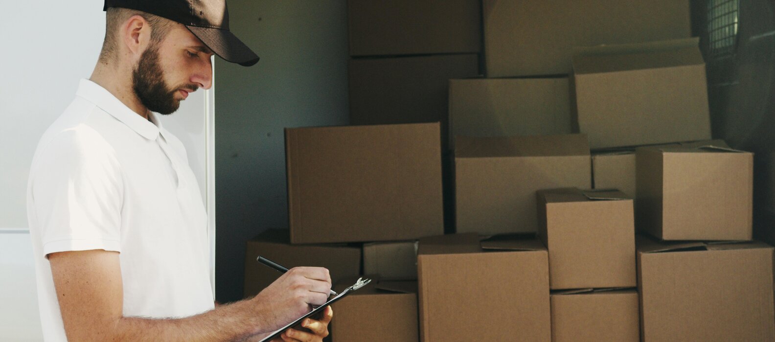 Mann überprüft den Versand von Kartons mit einem Klemmbrett.