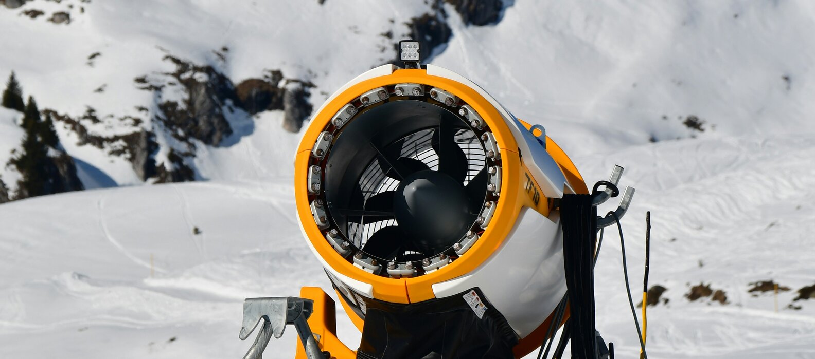 Schneekanone auf verschneitem Berg mit blauem Himmel im Hintergrund.