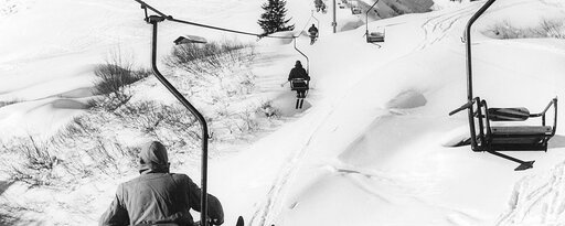 A chairlift glides over a snow-covered mountain landscape as skiers ride in the seats.