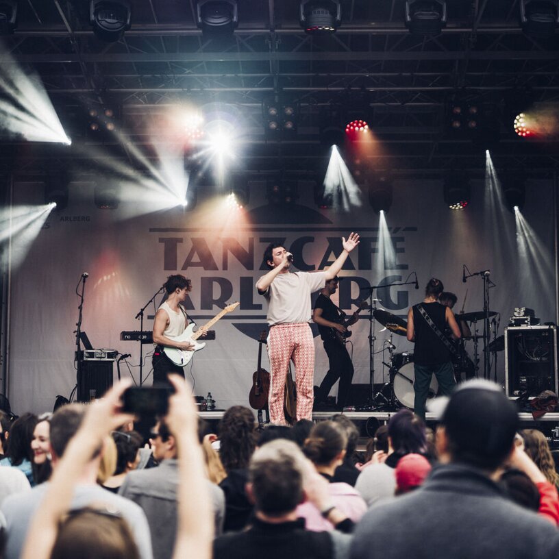 Band performing on stage in front of a crowd at Tanzcafè Arlberg music festival.