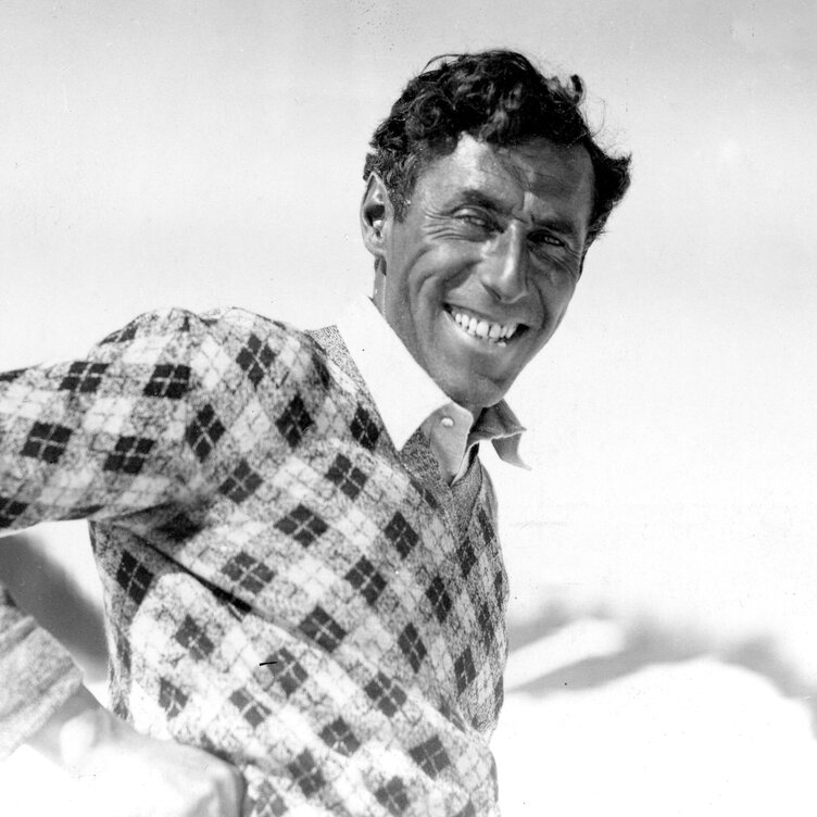 A man smiling in a checkered sweater against a bright background.