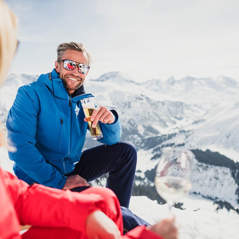 Man in blue jacket drinking beer in the mountains during spring skiing.