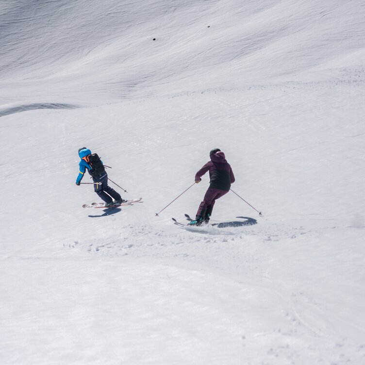 Two skiers in the sunshine skiing off piste.